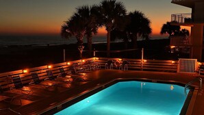 Piscina com espreguiçadeiras e vista para o oceano ao pôr do sol.