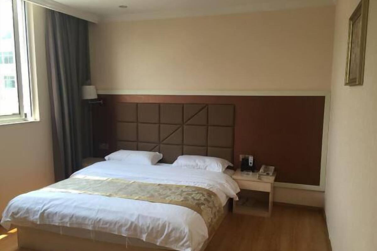 Una habitación de hotel con una cama grande, una mesita de noche con lámpara y una ventana con cortinas.