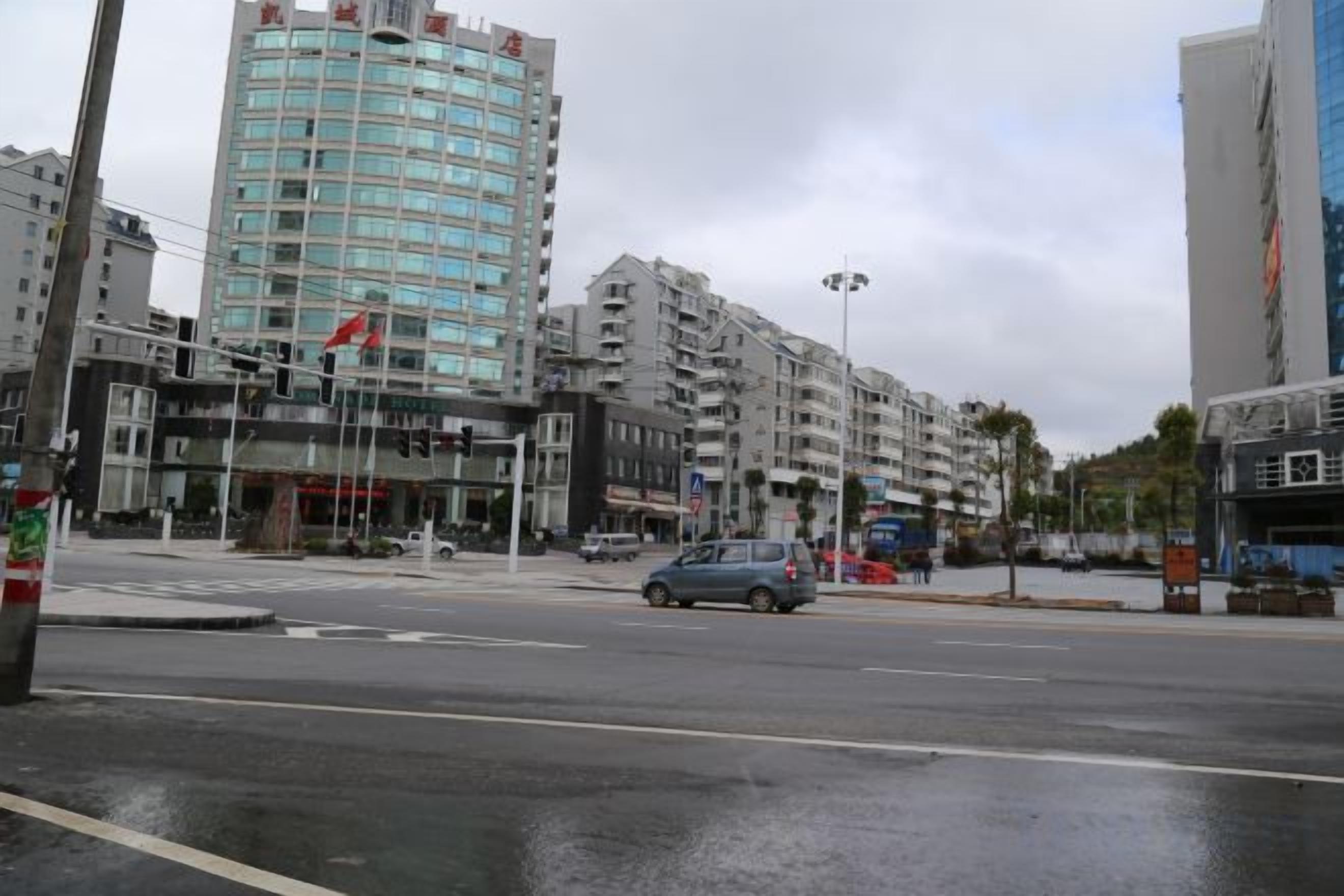 Un edificio de varios pisos con diseño moderno, situado en una intersección urbana con el pavimento mojado.