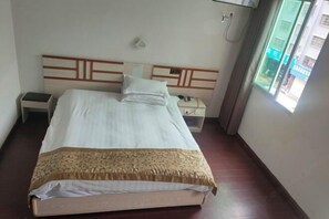 Una habitación de hotel con cama, mesitas de noche, teléfono y ventana.