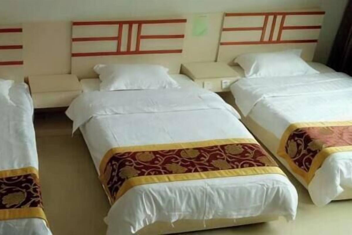 Habitación de hotel con tres camas individuales, cada una con cabecera y almohada.