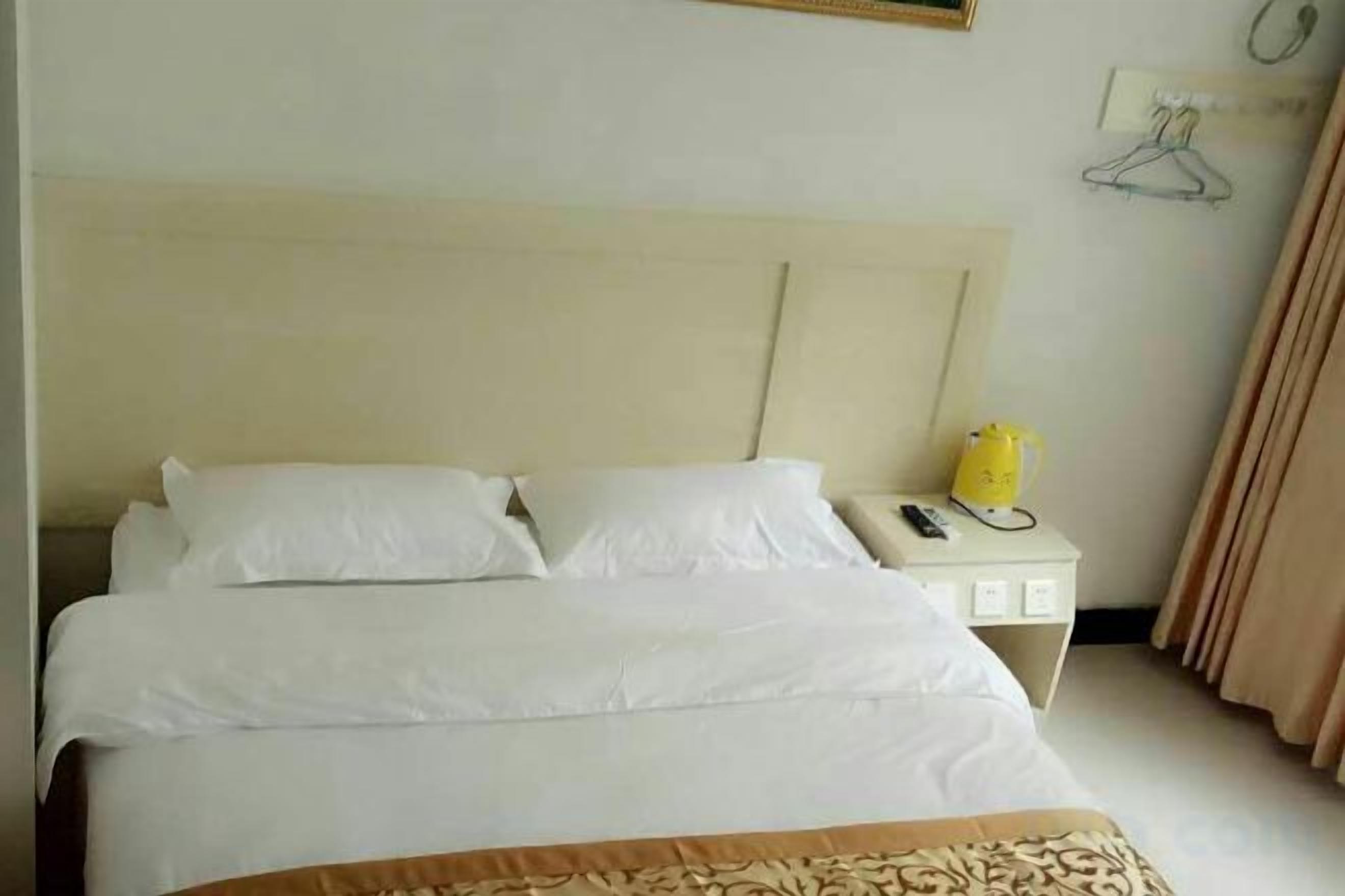 Una camera d'albergo con un letto, un comodino con un telefono e un oggetto giallo, e un'opera d'arte appesa al muro.