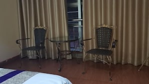 A hotel room with a bed, two chairs, a small table, and a view of a balcony through curtains. - pingnanxianbaoshanbibgguan (Pingnan)