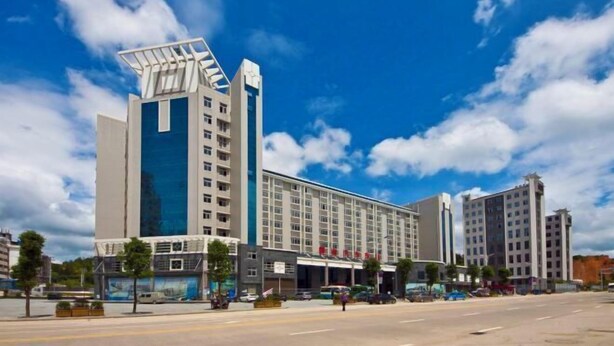 A modern hotel with a prominent glass facade, multiple floors, and a distinctive rooftop structure. - pingnanxianbaoshanbibgguan (Pingnan)