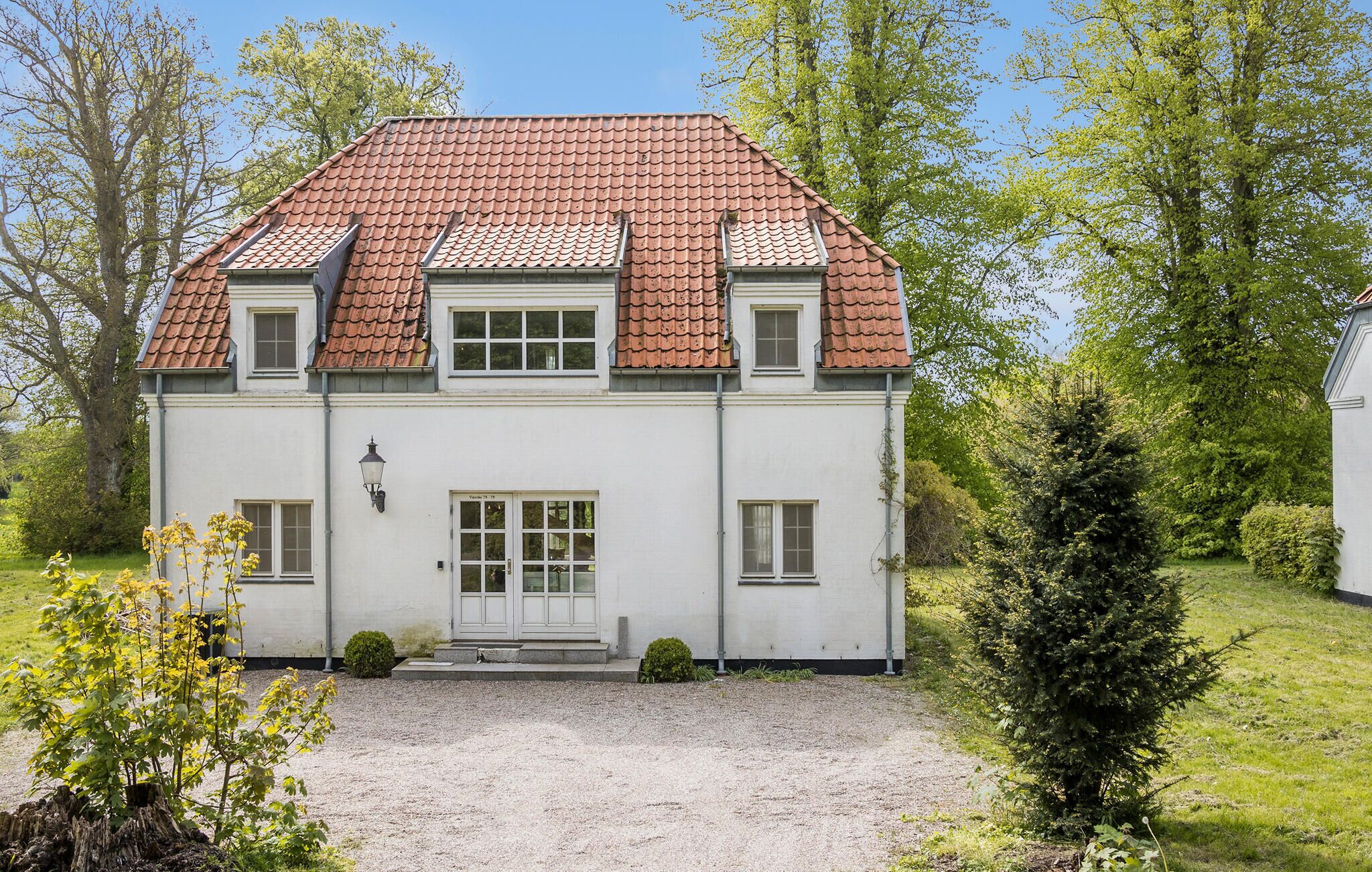 A two-story building with a red-tiled roof, white walls, and a gravel driveway.