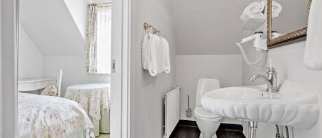 A bathroom with a white sink, a toilet, and a shower area. There is a mirror with a gold frame, and towels are hung on the wall.