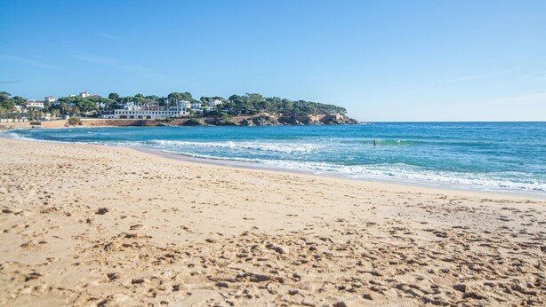 A sandy beach with footprints leading to the water, a clear sky, and buildings in the background. - Beach front home in Platja d'Aro with WiFi (Platja d'Aro)