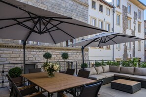 An outdoor patio with a wooden table, chairs, a sofa, and two umbrellas.