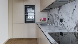 A modern kitchen with a built-in oven, a marble backsplash, and a stainless steel sink.