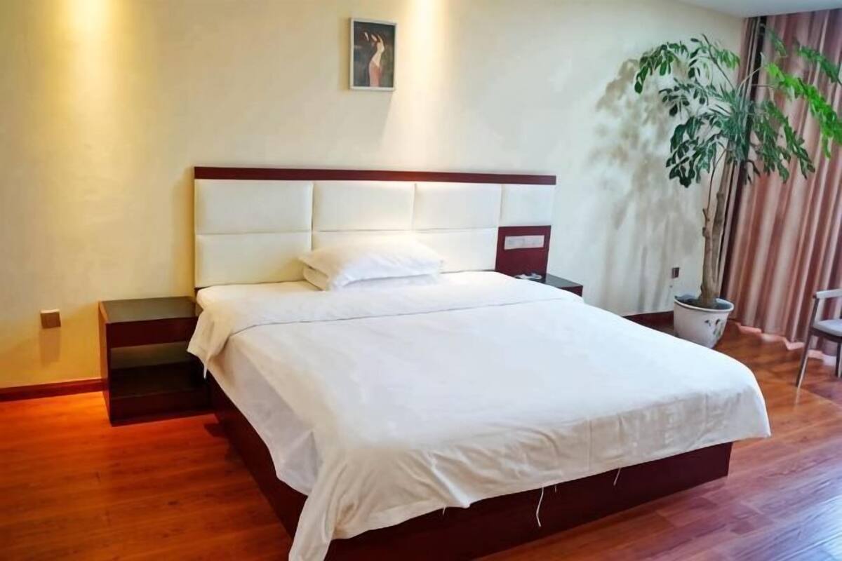 Een slaapkamer met een bed, nachtkastjes, een potplant en een stoel.
