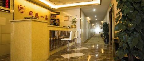 A hotel reception area with a marble floor, a reception desk, and a potted plant.
