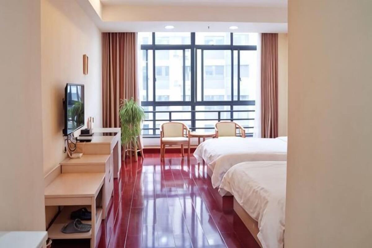 Een hotelkamer met een bed, een bureau met een televisie, een stoel en een groot raam.