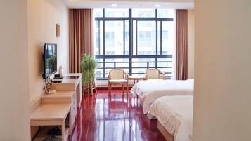A hotel room with a bed, a desk with a TV, a chair, and a large window.