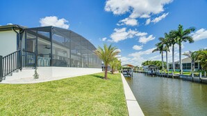Un bâtiment moderne doté d’une façade en verre, d’une zone verdoyante et d’un canal bordé de palmiers.