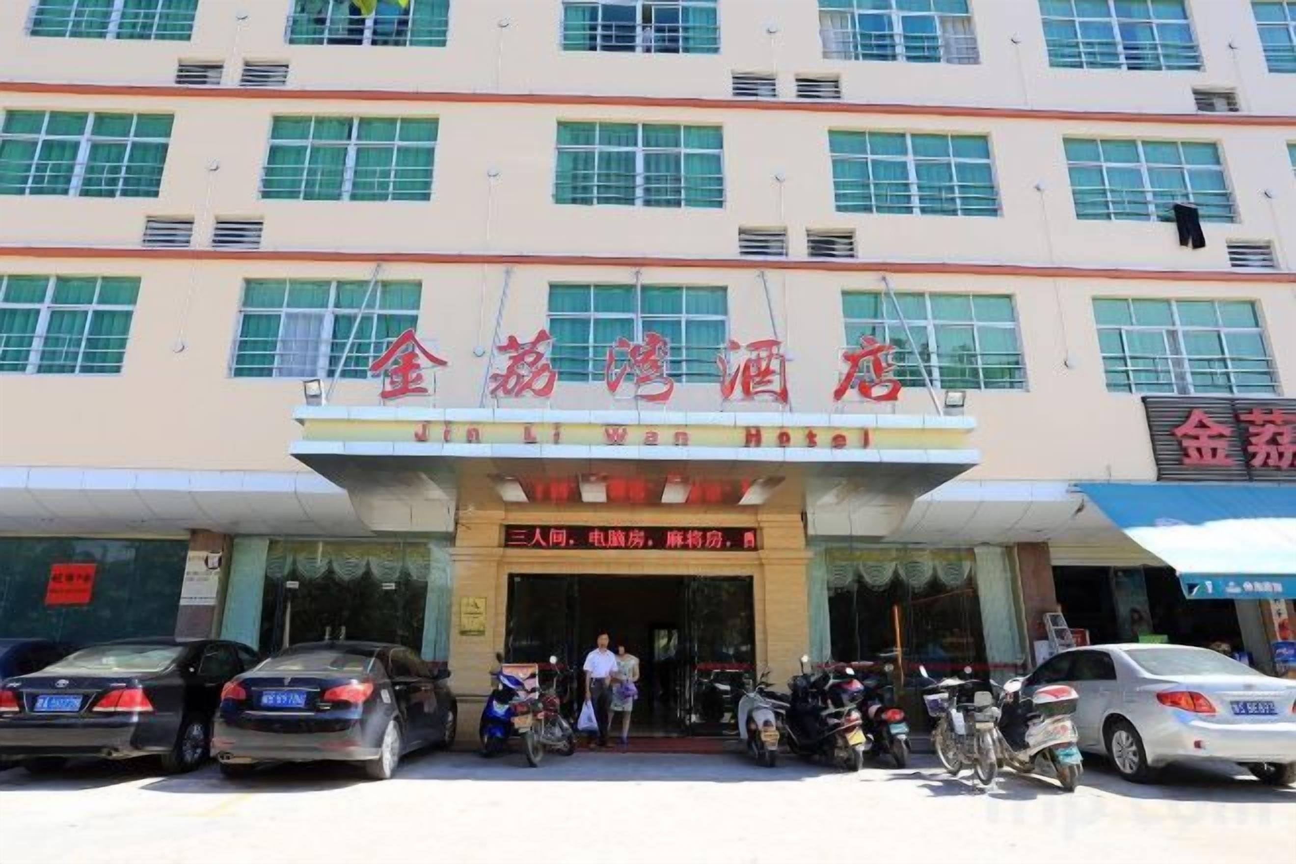 A hotel with a signboard, multiple windows, and parked vehicles.