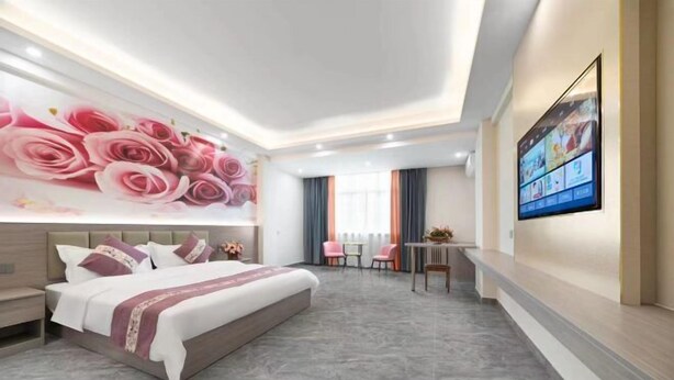 Een moderne hotelkamer met een groot bed, een televisie aan de muur, een bureau en een zithoek met stoelen.