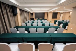 A conference room with rows of tables and chairs, a projector screen, and a stage area. - Xinhua Hotel Nanchuan (Chongqing)