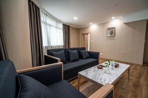 Ein modernes Wohnzimmer mit einem dunklen Sofa, einem Marmortisch und Blick auf eine Stadtkulisse durch große Fenster.