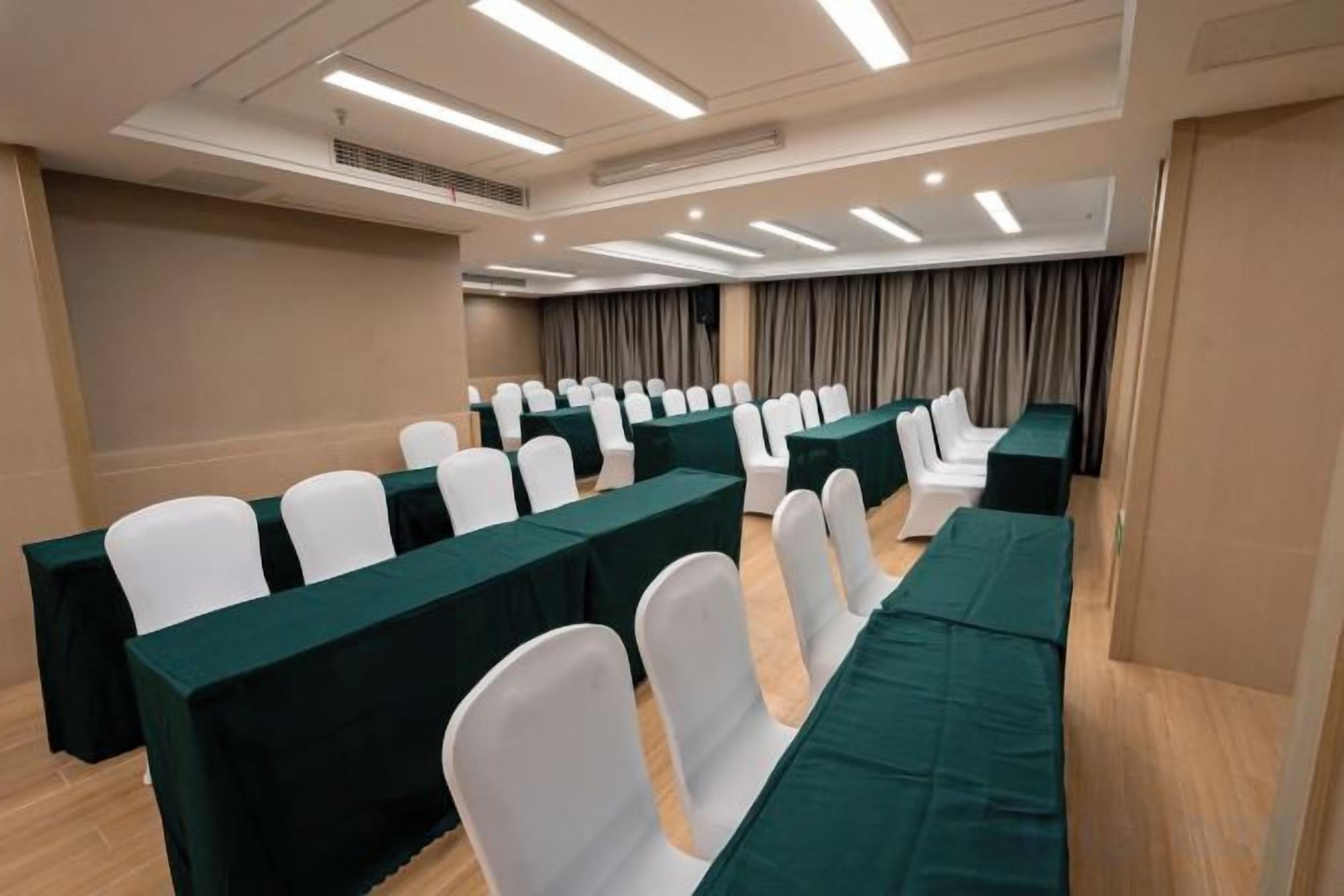 Une salle de conférence avec des rangées de chaises blanches, des nappes vertes et une décoration aux couleurs neutres.