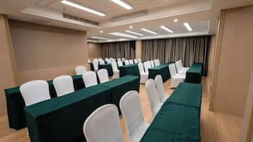 Une salle de conférence avec des rangées de chaises blanches, des nappes vertes et une décoration aux couleurs neutres.
