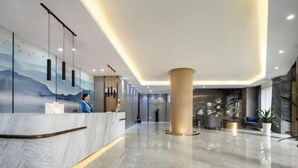 A modern hotel lobby with a marble reception desk, a large central column, and a mural on the wall. - Xinhua Hotel Nanchuan (Chongqing)