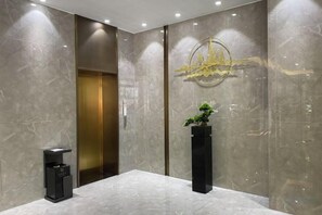 En modern entréhall med ett marmorgolv, en receptionsdisk, en krukväxt och en väggmonterad lampa.