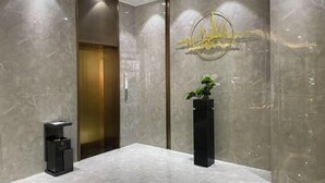 A modern lobby with a marble floor, a reception desk, a potted plant, and a gold elevator. - Xinhua Hotel Nanchuan (Chongqing)