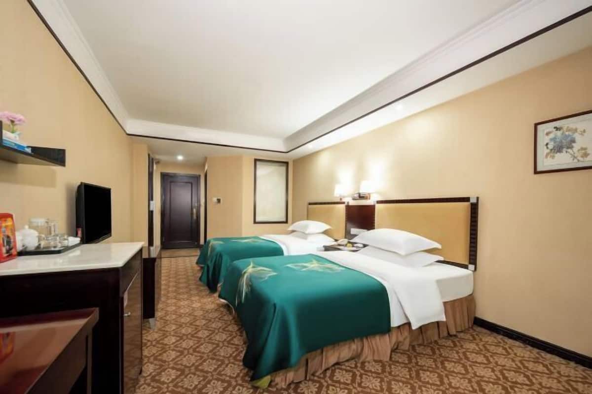 Ein Hotelzimmer mit zwei Betten, einem Schreibtisch, einem Fernseher und einer Tür zu einem weiteren Raum.