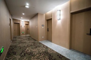 En hotellkorridor med heltäckningsmatta på golvet, dörrar och väggmonterade lampor.