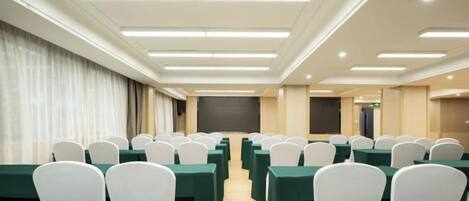 A conference room with rows of tables and chairs, a projector screen, and a stage area.