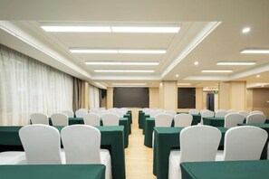 A conference room with rows of tables and chairs, a projector screen, and a stage area.