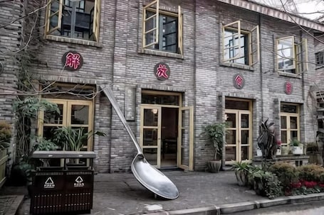A brick building with multiple doors and windows, some with open shutters, and a large spoon-like object on the ground.. Xinhua Hotel Nanchuan