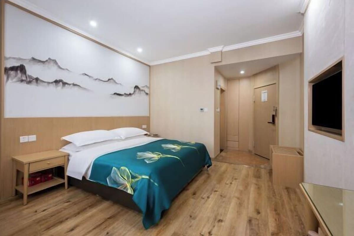 Ein Hotelzimmer mit einem Bett, einem Nachttisch, einem an der Wand montierten Fernseher und einer Tür zu einem anderen Raum.