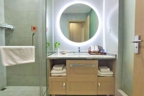 Ein modernes Badezimmer mit rundem Spiegel, Handtuchhalter und Waschbecken mit Pflegeprodukten.
