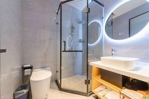 Un baño moderno con ducha de vidrio, lavamanos blanco y espejo redondo.