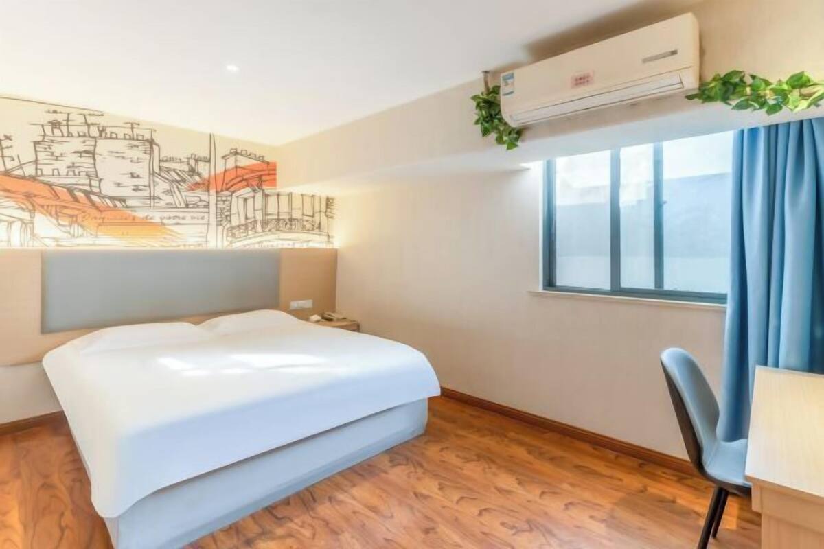 Een kamer met een bed, een bureau, een stoel, een airconditioning en een raam met gordijnen.