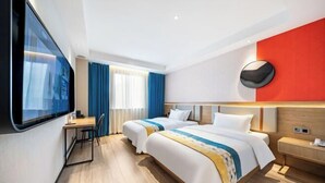 Habitación de hotel con dos camas, un escritorio, una silla, un televisor montado en la pared y un amplio ventanal con cortinas.