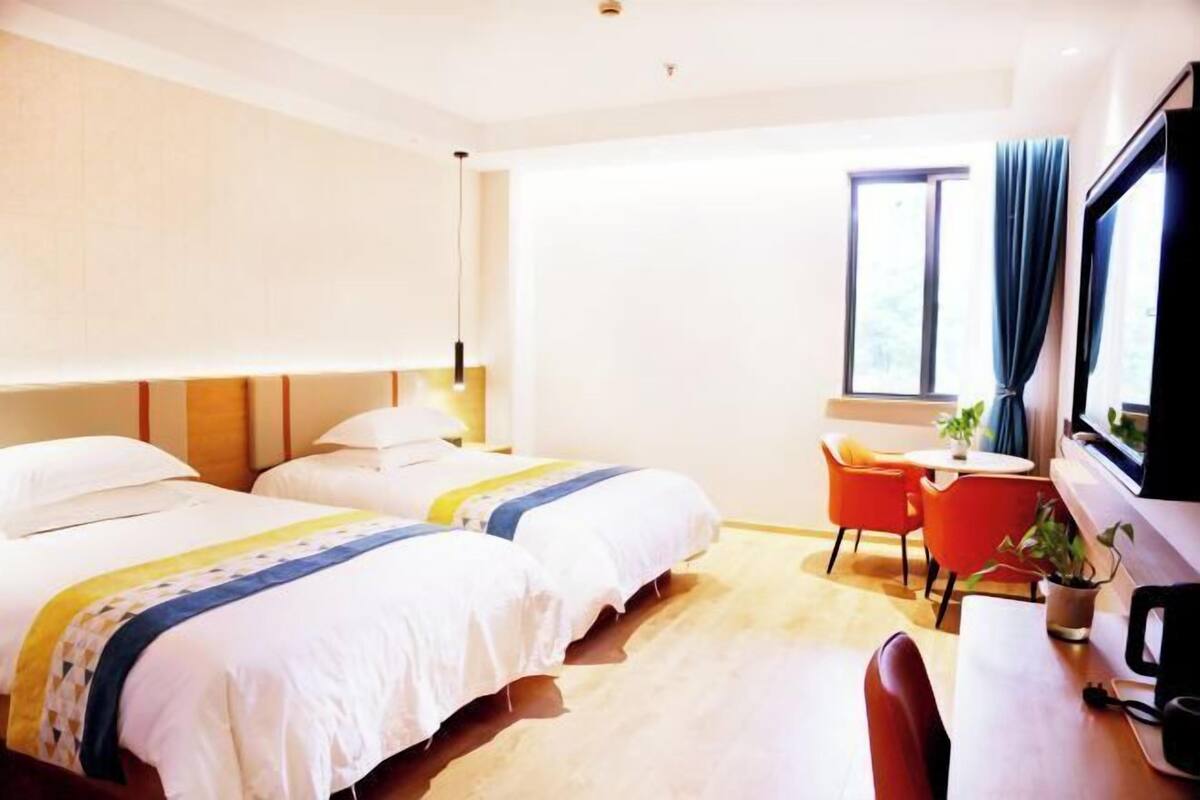 Hotelkamer met twee bedden, een bureau, een stoel, een televisie en een raam met gordijnen.