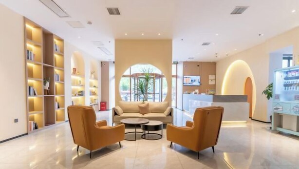 Un moderno vestíbulo de hotel con un sofá, dos sillones, una mesita de centro y una estantería.