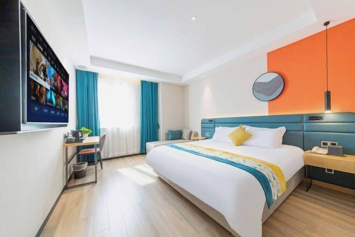 Een hotelkamer met een groot bed, een bureau met stoel, een aan de muur bevestigde televisie en een raam met gordijnen.