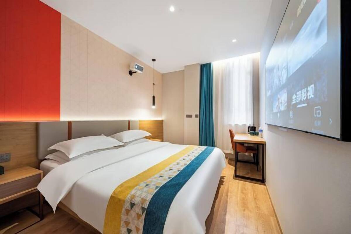 Een hotelkamer met een bed, een bureau, een stoel, een televisie en een projectiescherm.