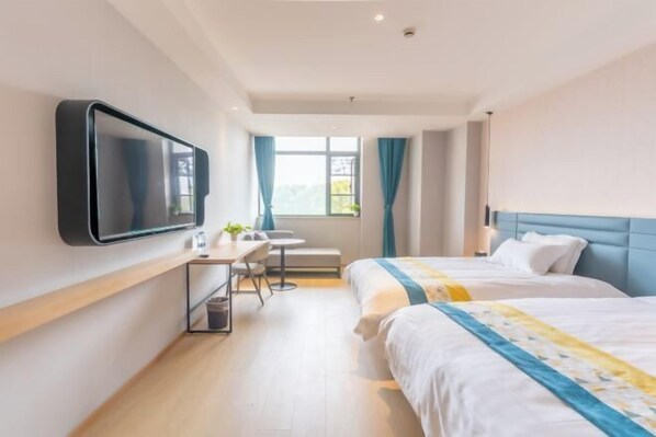 Una habitación de hotel con dos camas, un escritorio, una silla, un televisor montado en la pared y una ventana con cortinas.