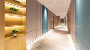 Un pasillo moderno de hotel con paneles de madera, iluminación empotrada y plantas en macetas.