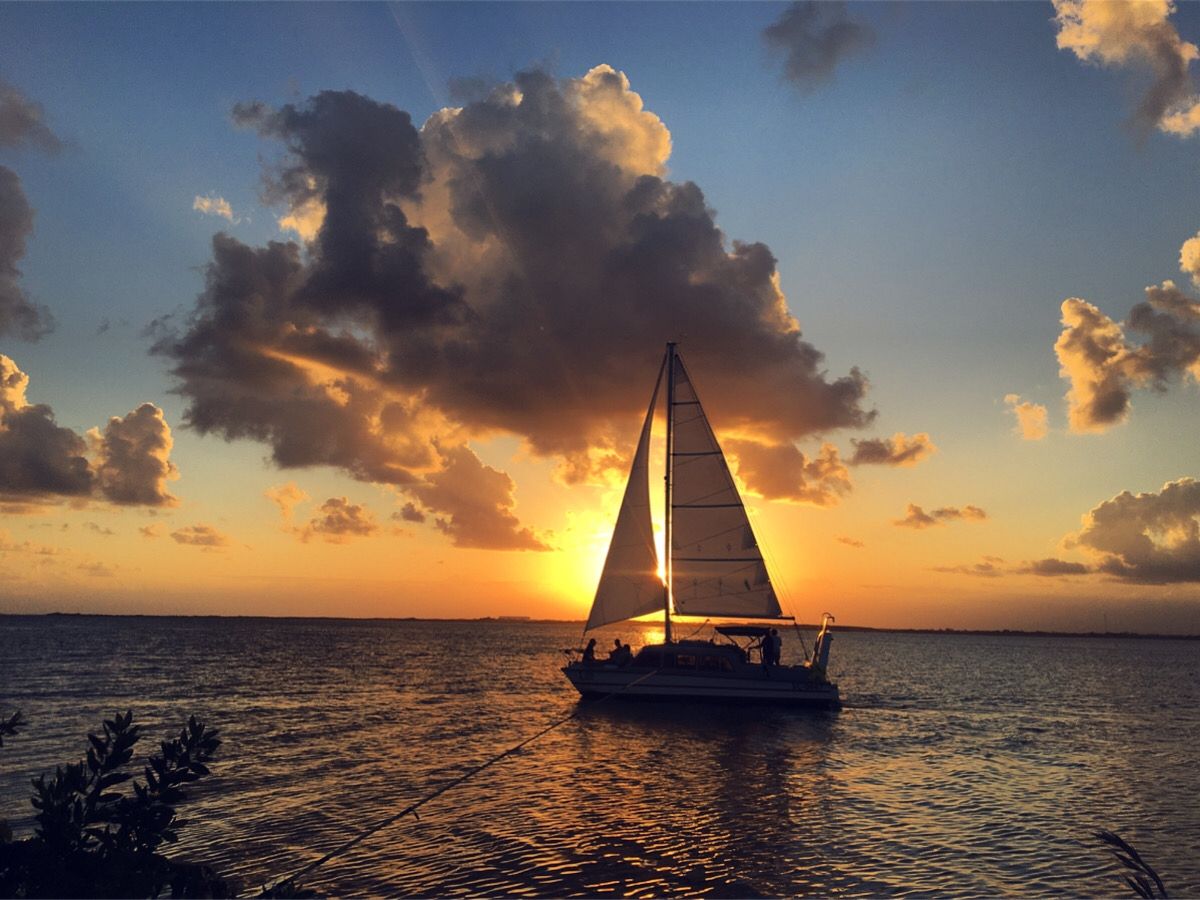 A sailboat on calm waters during sunset with a clear sky.