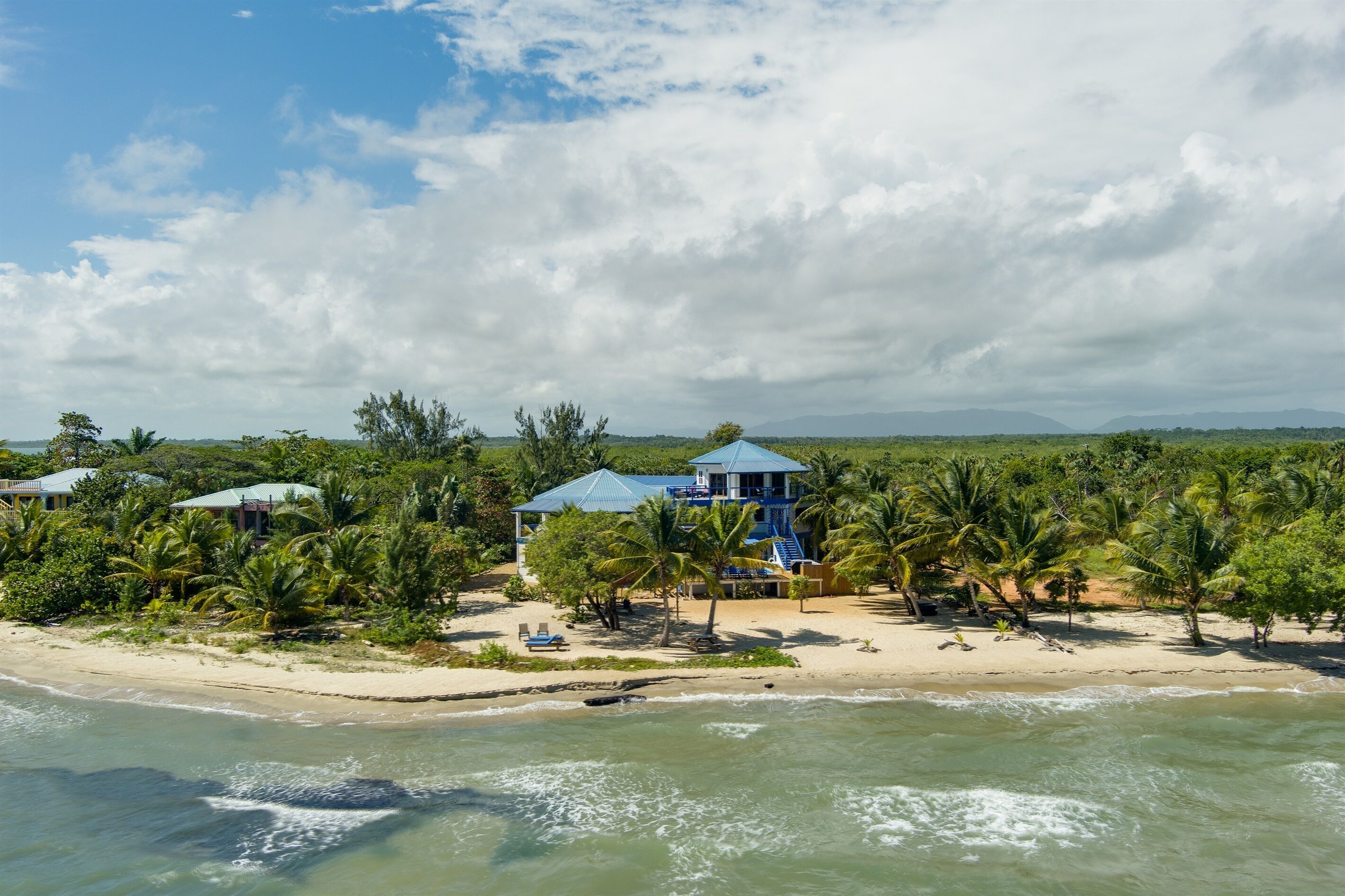 A beachfront property with a large blue building, palm trees, and a sandy beach.