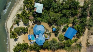 An aerial view of a beachside property with a swimming pool, umbrellas, and a large blue-roofed building.