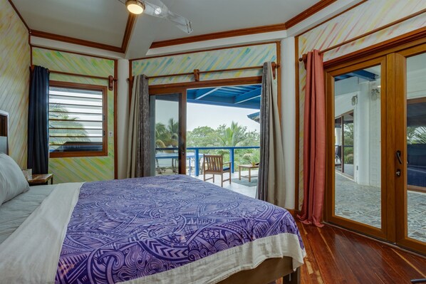 Une chambre avec un lit, une fenêtre avec des rideaux, un balcon avec une chaise et une vue sur l’extérieur.