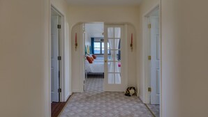 Un couloir mène à une chambre où se trouvent un lit, une fenêtre et un chat sur le sol.