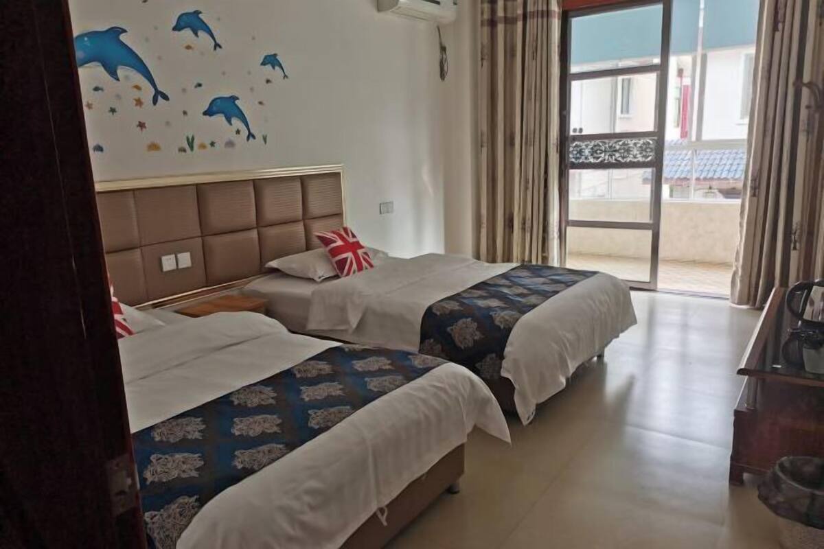 A hotel room with two beds, a window with curtains, a wall with dolphin decals, and a view of the outside.