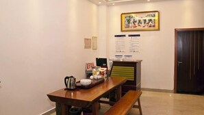 Una habitación con una mesa de madera, un banco, una tetera y una bandeja con alimentos. Hay un cuadro en la pared y una puerta al fondo.